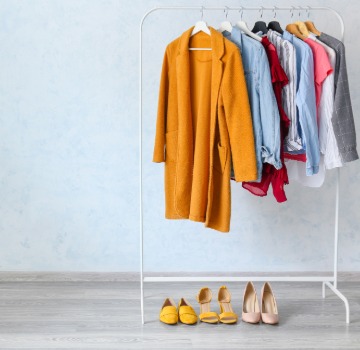 a clothing rack with eight pieces of clothing hanging on it, a mustard sweater, blue button down shirt, a red dress, a jean jacket, a black blazer and three short sleave shirts